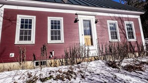 Una casa rossa con rifiniture bianche, un camino e una finestra con una campana laterale.