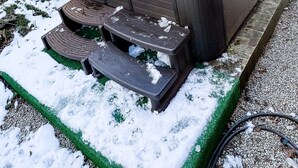 Una vasca idromassaggio su una piattaforma di legno con gradini, circondata da neve e un vialetto sterrato.