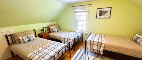 Ein Zimmer mit zwei Betten, einem Fenster mit Jalousien, einer Deckenleuchte und einem gerahmten Bild an der Wand.