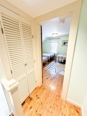A hallway leading to a bedroom with a bed, a window, and a door with louvered shutters.
