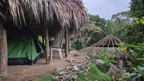A thatched-roof hut with a green tent nearby, surrounded by rocks and greenery. - La Cima Tayrona (Santa Marta)