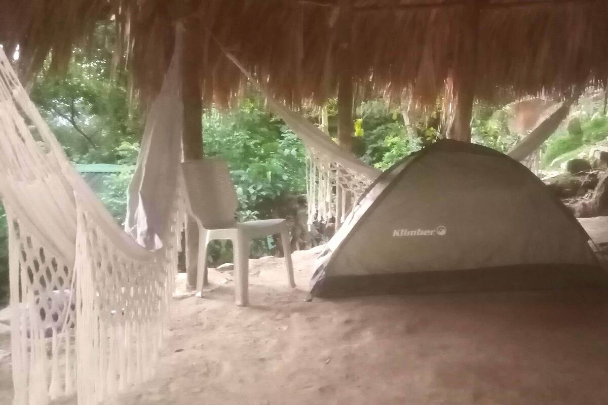 A tent labeled 'Klimber' in a natural setting with a thatched roof and a chair nearby.