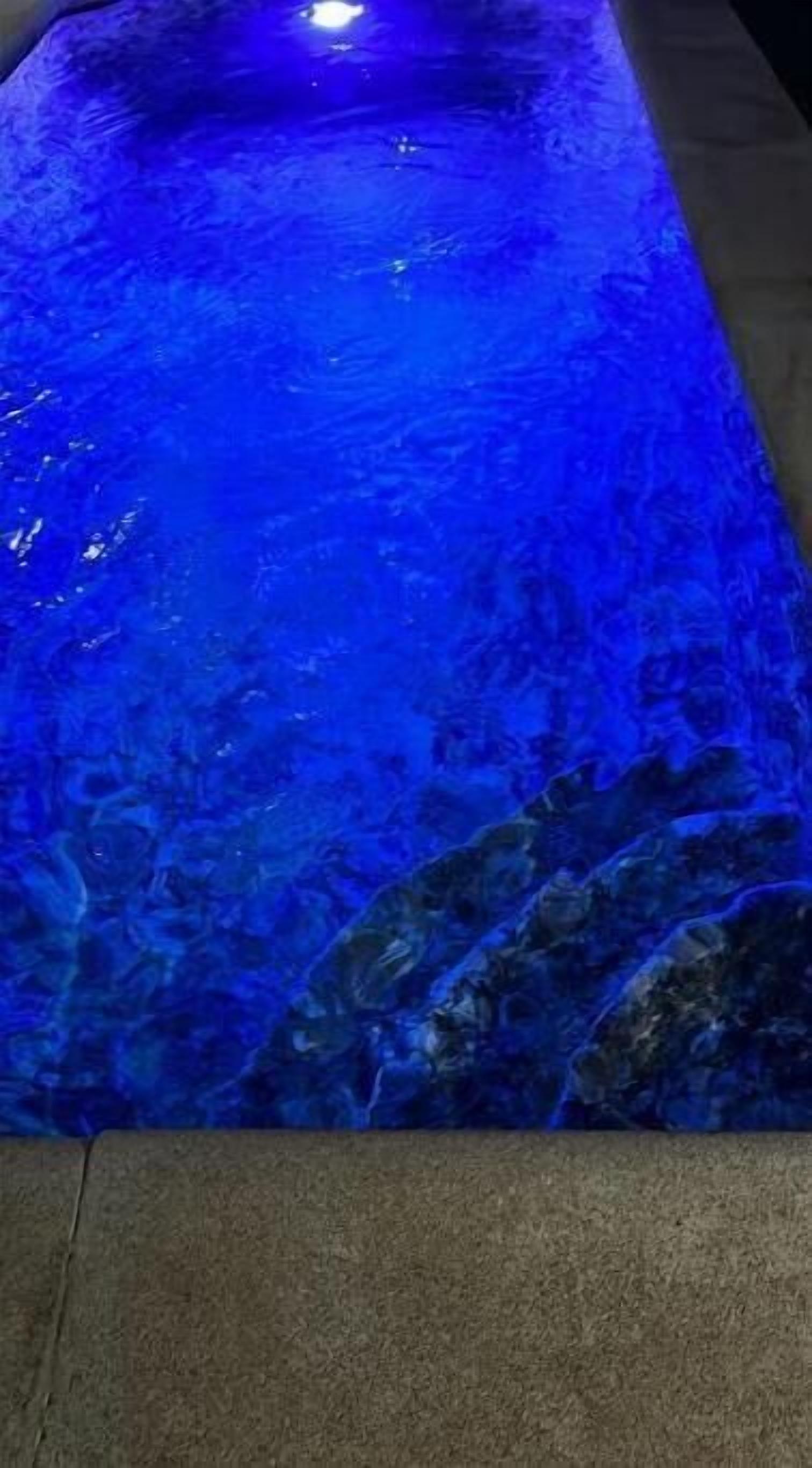 A long, narrow pool with a blue, reflective surface and a stone border.