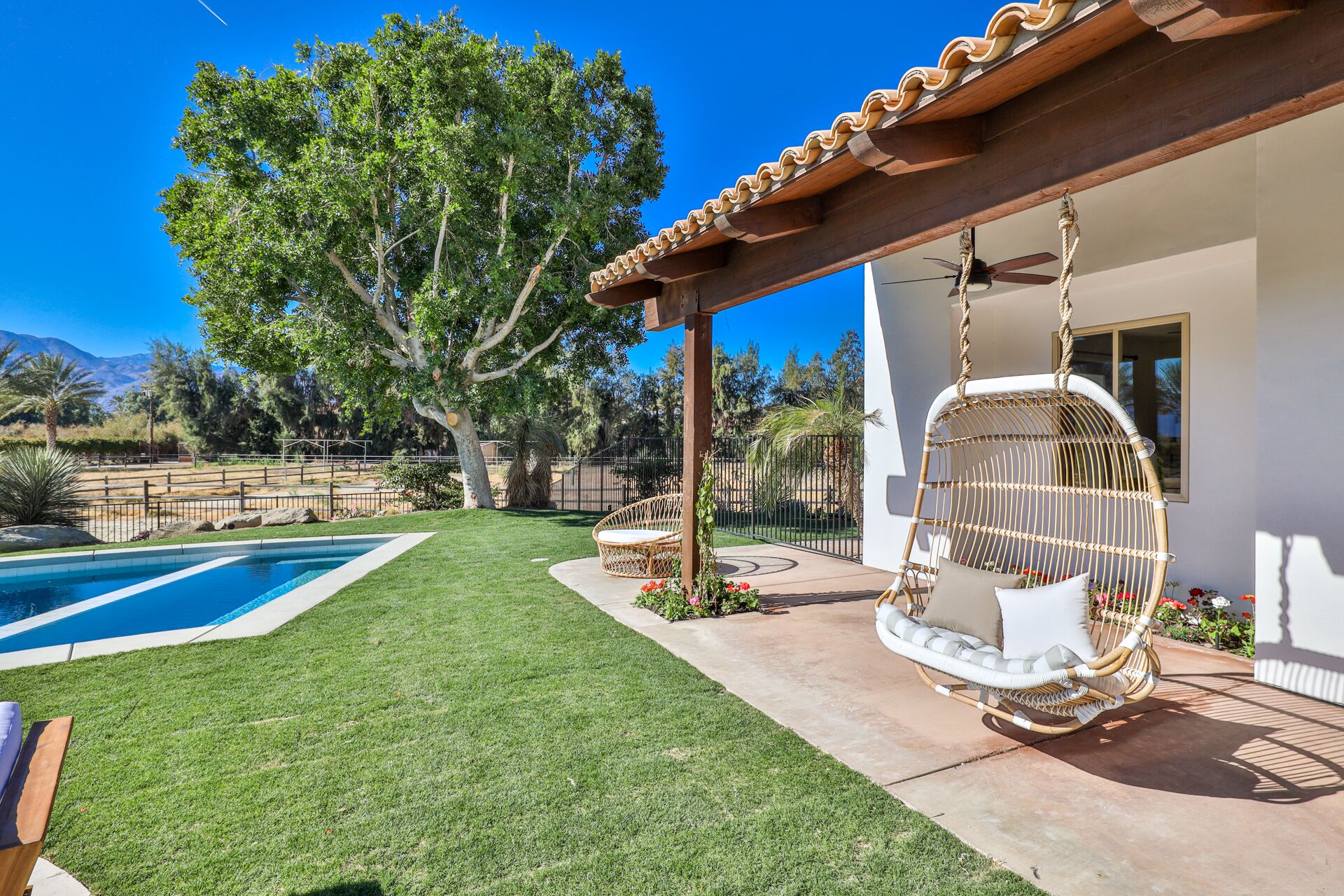 Un patio trasero con piscina, una silla colgante y una pérgola.