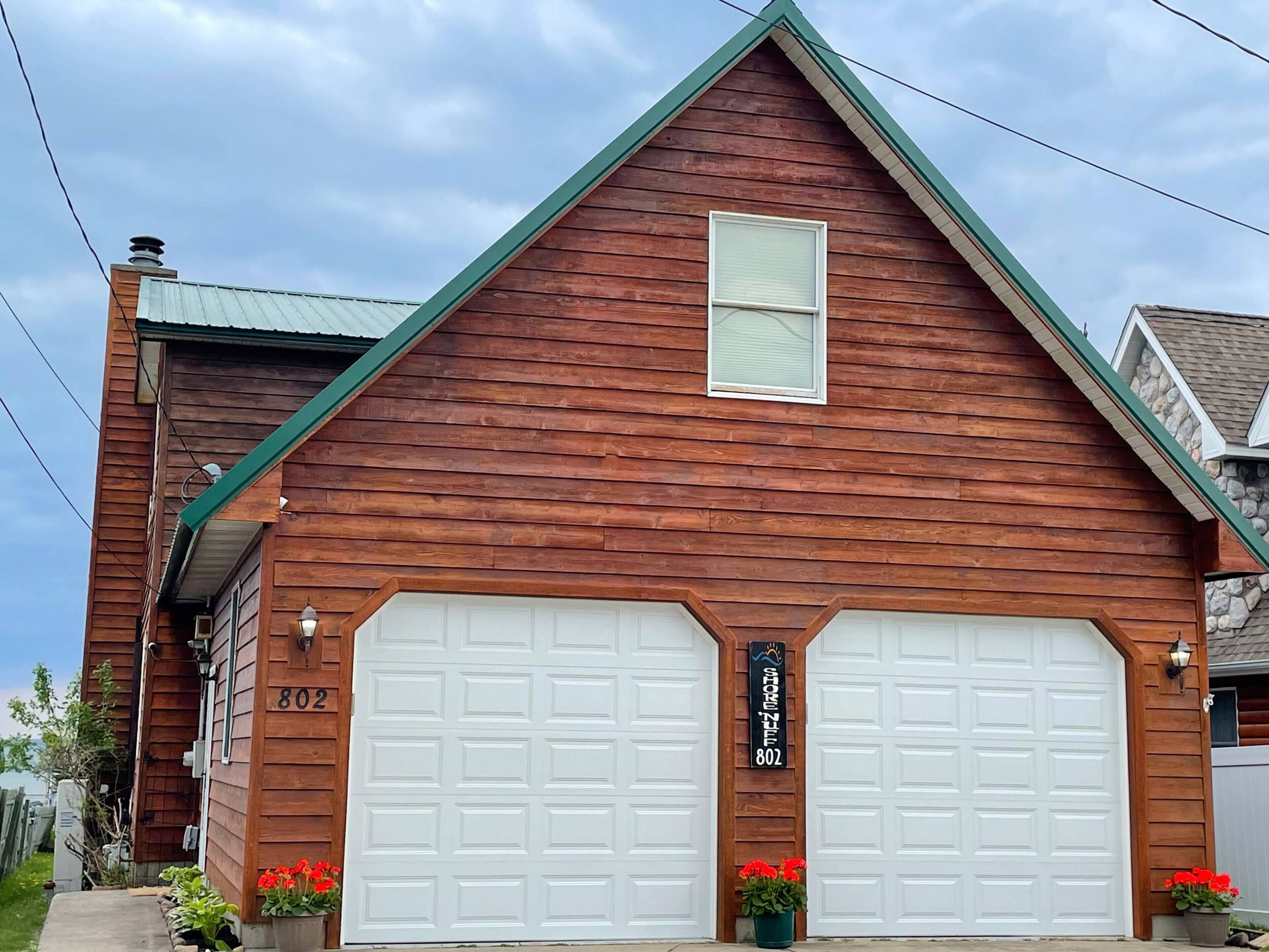 A two-story wooden house with a green roof, two garage doors, and a small window.