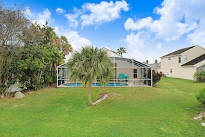 Ein Haus mit überdachtem Pool, Rasen und einer Palme.