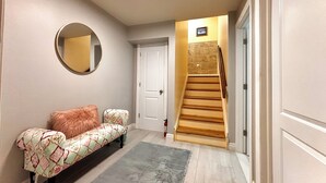 A hallway with a wooden staircase, a round mirror, a patterned sofa, and a gray rug. - Cozy Ski On/Off Condo Located at Hunter Mountain (Hunter)