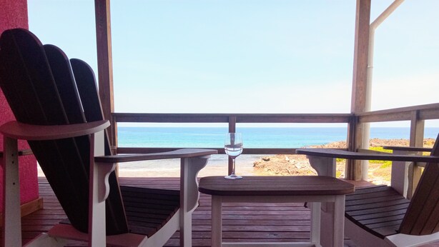 Een houten terras met een tafel en stoelen met uitzicht op een strand.
