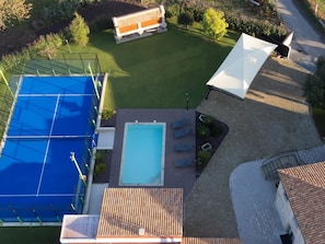 Ilmakuva kiinteistöstä, jossa on uima-allas, tenniskenttä ja ulkotila, jossa on patio ja ulkokalusteita.
