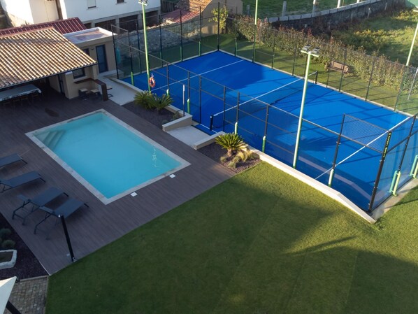 A swimming pool with a blue cover, surrounded by a fence, and adjacent to a building with outdoor seating.