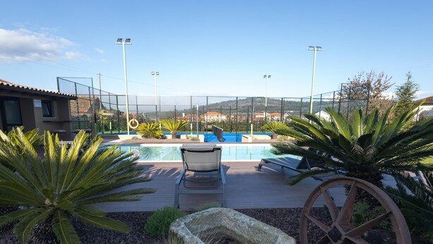 Zona de piscina con vistas a las montañas, rodeada por una cerca, que incluye un macetero de piedra y una rueda antigua.
