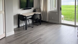 A modern living room with a flat-screen TV mounted on the wall, a dining table with chairs, and a large sliding glass door leading to a grassy outdoor area. - Lakefront Studio Condo~Step into the Lake at Spader Bay (Chelan)