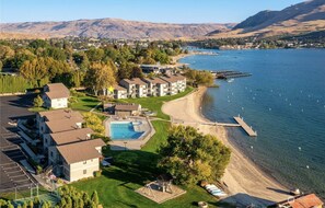 A coastal hotel with a swimming pool, beach access, and a view of the lake and mountains.