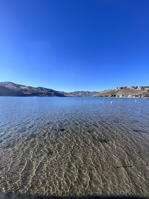 A clear lake with visible underwater patterns and a distant town on the shore.