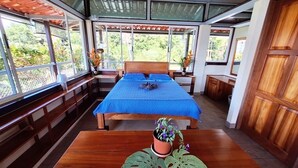 Quarto com cama, mobiliário de madeira e vista para o verde.