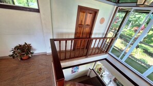 Interior com vários níveis, escada de madeira, uma porta e vista de um jardim através de grandes janelas.