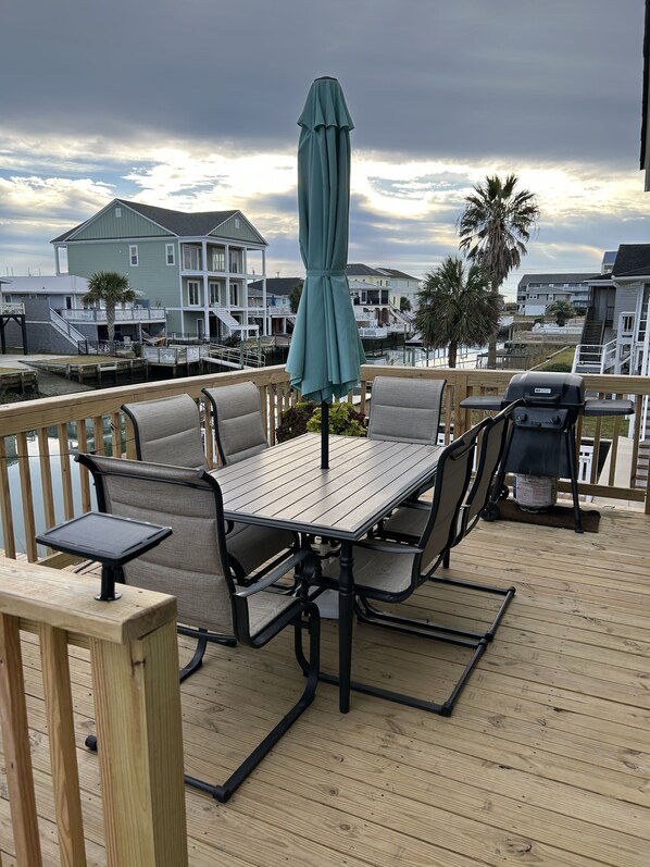 A wooden deck with a table and chairs, an umbrella, and a grill. - New Pool + Putting Green, Walk to Beach, Waterfront Home in Cherry Grove! (North Myrtle Beach)