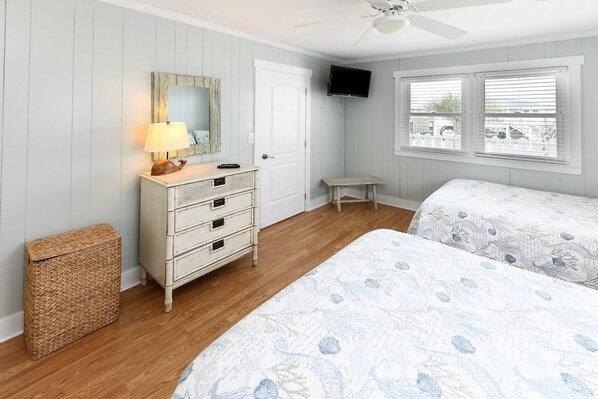 A bedroom with two beds, a dresser, a television, and a ceiling fan.