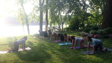 A group of people performing yoga on mats in an outdoor setting with trees and a body of water in the background.