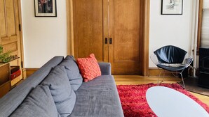 A living room with a grey sofa, red cushion, wooden wardrobe, and a red rug. - Victorian Modern, on the Mississippi River (Minneapolis)