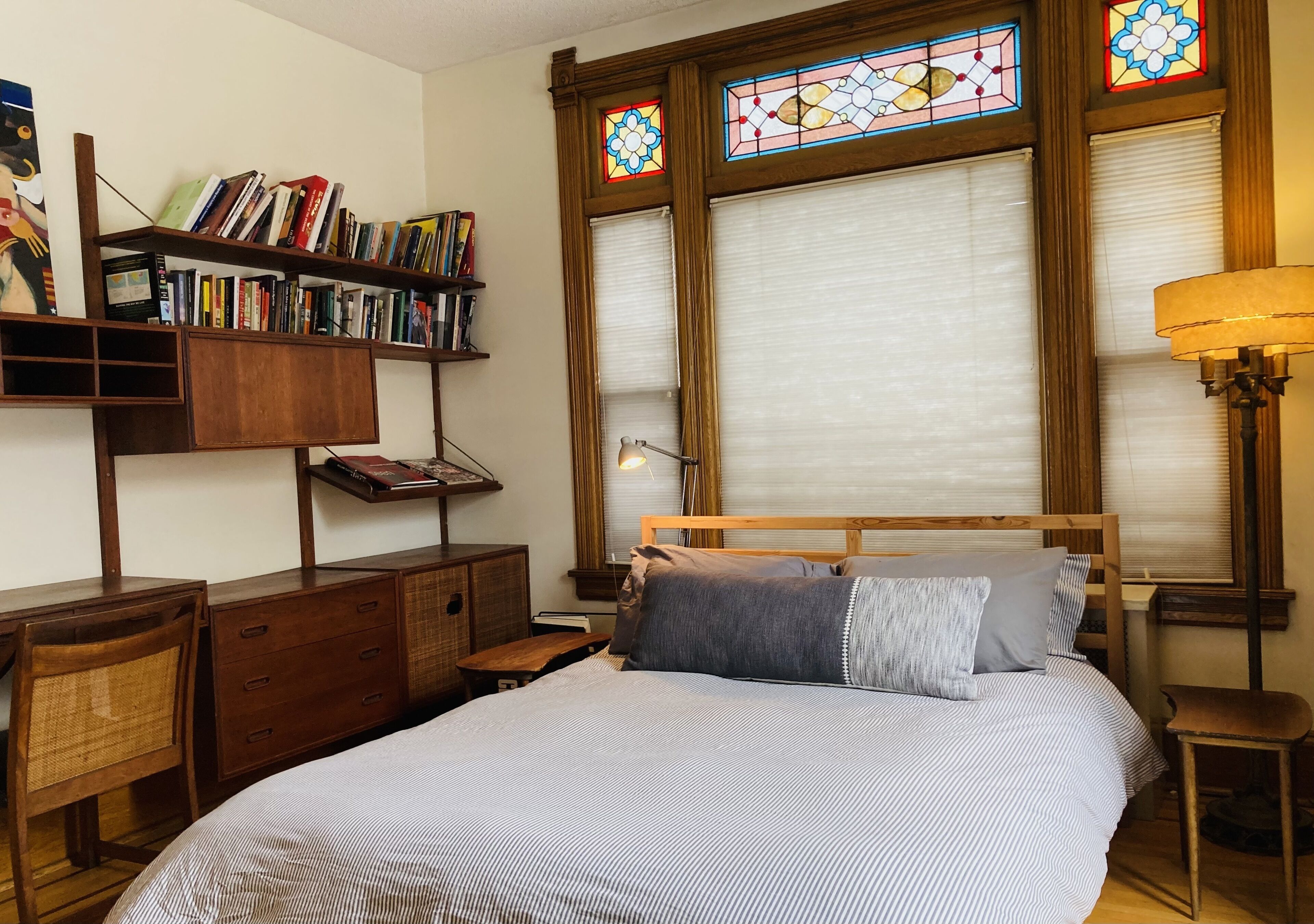 A bedroom with a large bed, wooden headboard, a bookshelf, and a window with stained glass.