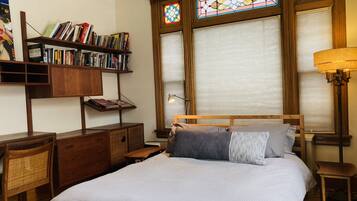 A bedroom with a large bed, wooden headboard, a bookshelf, and a window with stained glass.