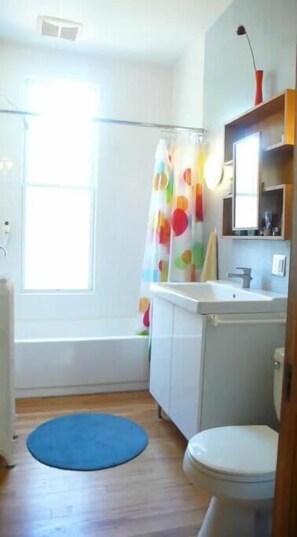 A bathroom with a shower curtain, a sink, a toilet, and a blue mat on the floor. - Victorian Modern, on the Mississippi River (Minneapolis)