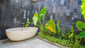 A modern bathroom with a freestanding bathtub, tiled walls, and lush greenery. - 3 br villa across from Thomas beach, Uluwatu . (Pecatu, Bali)