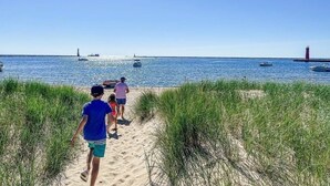 Un sendero arenoso que lleva al mar, con barcos y un faro a lo lejos.