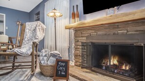 Una sala de estar acogedora con chimenea, un sillón mecedor, una cesta y un cartel que dice 'Keep Cozy'.