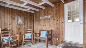 Un porche de madera con mecedoras y piso de piedra, una puerta con felpudo que dice 'Welcome', y un cartel que dice 'Michigan'.
