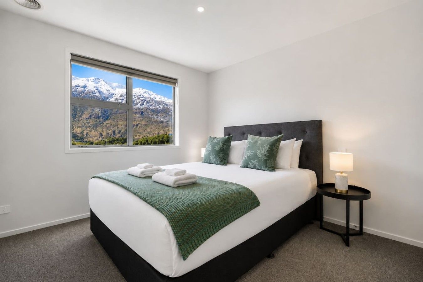 A bedroom with a bed, pillows, a bedside table with a lamp, and a window with a mountain view.