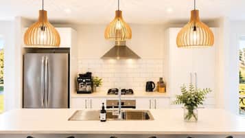 A modern kitchen with a stainless steel refrigerator, a gas stove, and a sink. There are three pendant lights hanging above the counter.