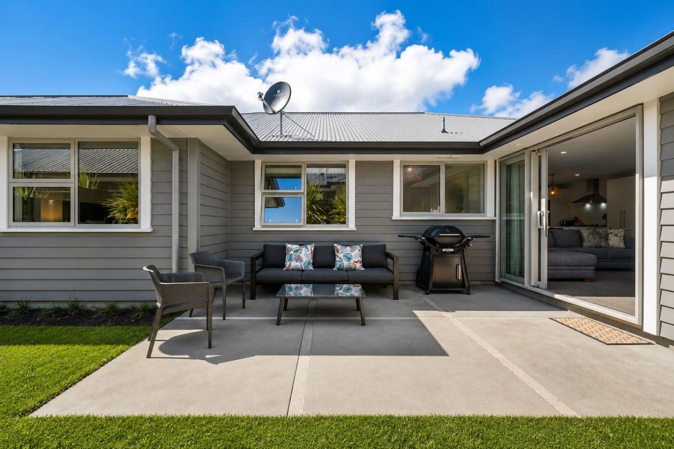 A modern house with a patio, outdoor seating, and a sliding glass door leading to a living area.