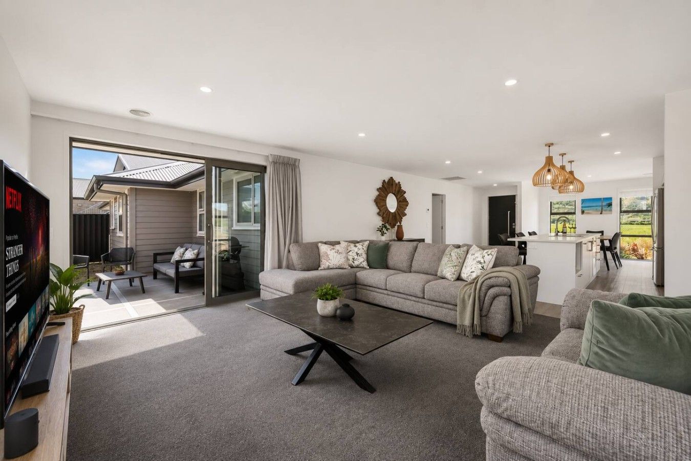 A modern living room with a sofa, coffee table, and a TV. There is a sliding glass door leading to an outdoor area.