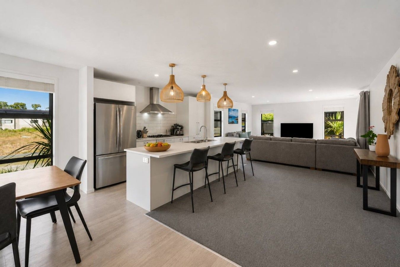 Une cuisine moderne dotée d’un îlot central, d’appareils électroménagers en acier inoxydable et de luminaires suspendus.