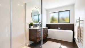 Ein modernes Badezimmer mit Duschkabine aus Glas, einem Holzbadezimmermöbel, einem großen Spiegel, einer Badewanne und einem Fenster mit Tageslicht.