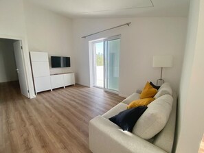 Una sala de estar moderna con un sofá, un televisor de pantalla plana y un puerta corrediza de vidrio que da a un balcón.