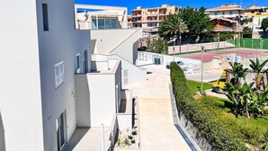 A modern building with a white facade, a visible staircase, and a sports field in the background. - AGATA PENTHOUSE KEYS: SEA VIEW (MODICA)