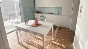 A modern kitchen with white cabinets, a white countertop, and a dining table with clear chairs. - AGATA PENTHOUSE KEYS: SEA VIEW (MODICA)