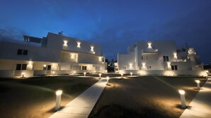 A modern building complex with multiple white structures, illuminated pathways, and evenly spaced bollards. - AGATA PENTHOUSE KEYS: SEA VIEW (MODICA)