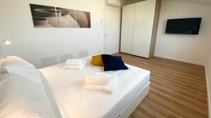 A modern hotel room with a large bed, a flat-screen TV, a painting on the wall, and a wardrobe. - AGATA PENTHOUSE KEYS: SEA VIEW (MODICA)