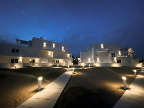 A modern building complex with multiple white structures, illuminated pathways, and evenly spaced bollards. - KEYS CORALLO: APARTMENT ON TWO LEVELS NEAR THE SEA!! (MODICA)