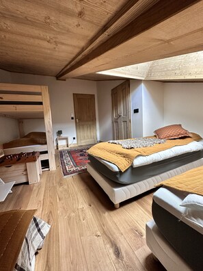 Cozy bedroom with a single bed, wooden bench, and laptop, set against a sloping ceiling with exposed beams.