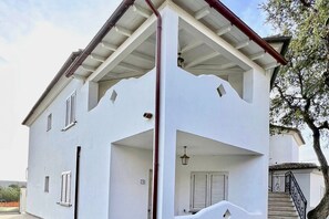 Un edificio de dos pisos con fachada blanca, un porche cubierto y una escalera que conduce al piso superior.