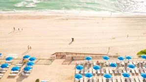 Una platja amb files de gandules i ombrel·les, una estructura de fusta i l'oceà al fons.