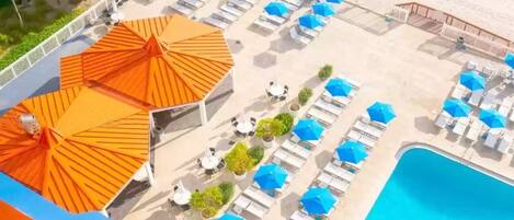An aerial view of a beachside resort with sun umbrellas, lounge chairs, and a swimming pool.