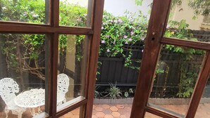 A view through a wooden-framed window into a garden area with a hexagonal tiled floor, white outdoor furniture, and lush greenery. - "Villa Magdalena" luxury studio (St Kilda)