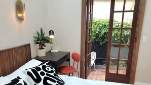 A bedroom with a bed, a desk with a lamp, a chair, and a view of the outdoors through a door. - "Villa Magdalena" luxury studio (St Kilda)