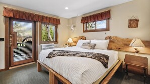 A bedroom with a large bed, wooden headboard, two bedside tables with lamps, a wooden bench, and a window with blinds.